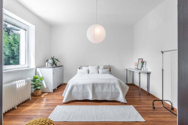 A bright bedroom with a bed, window, and houseplants in a two-room apartment.