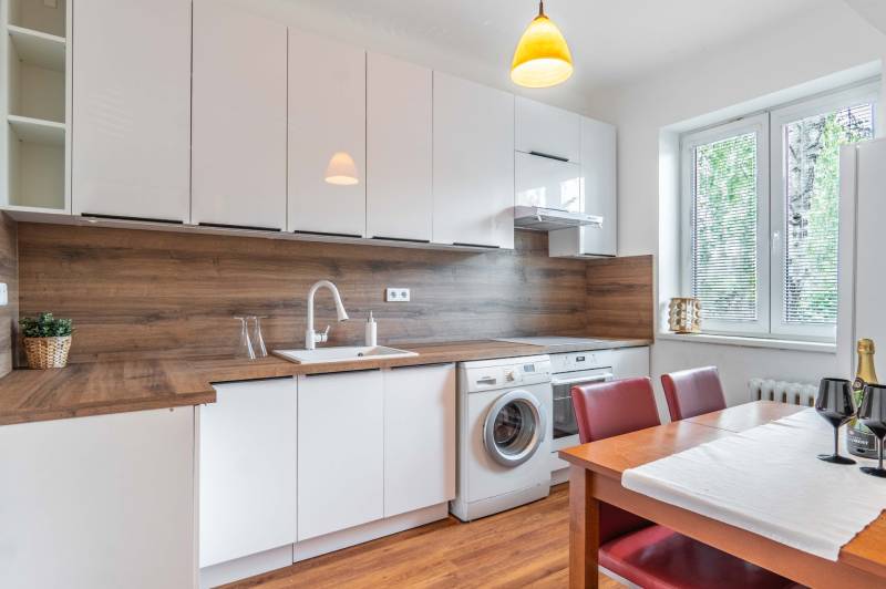A kitchen with a large window, dining table, washing machine, and wooden paneling in a 2-room apartment.