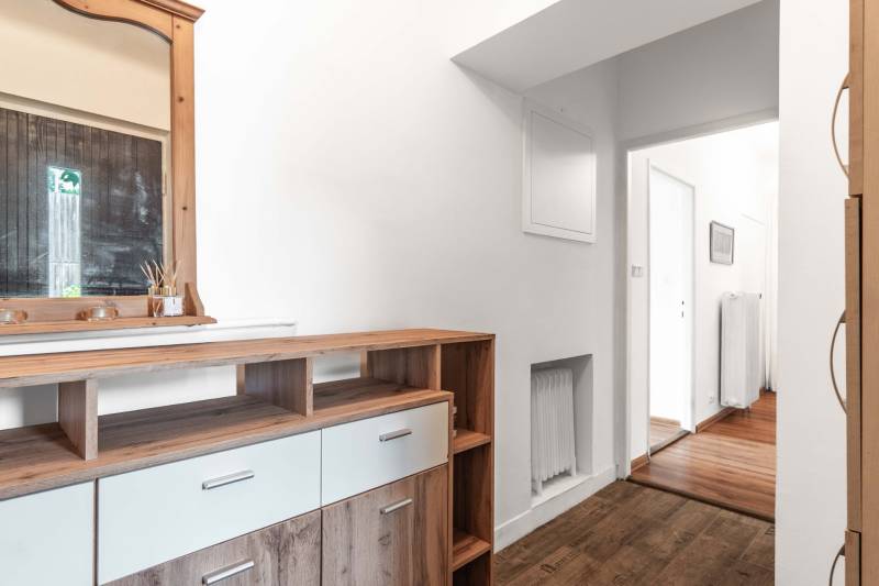 A dresser with a wooden mirror in the hallway of a two-room apartment, leading to a bright corridor.