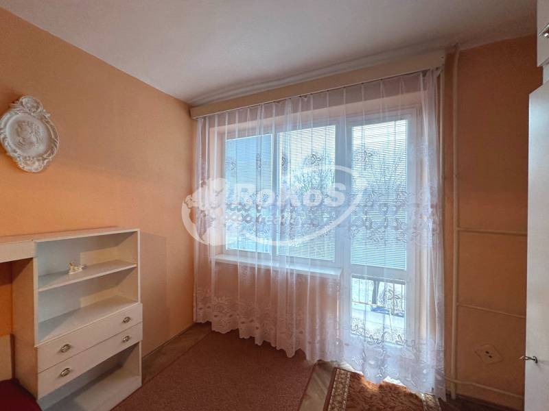 A room in a three-room apartment with orange walls and a white curtain on the window.