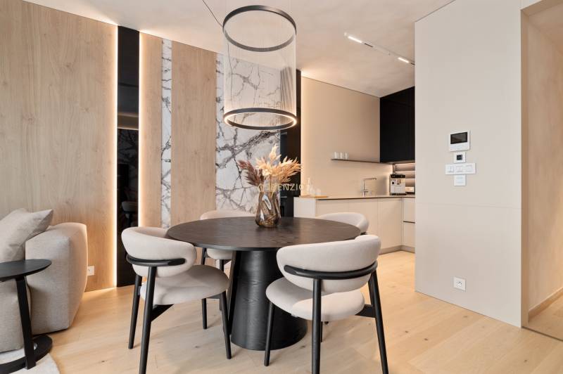 Dining room in a 3-room apartment with a round table, wooden decorations, and an open kitchen.