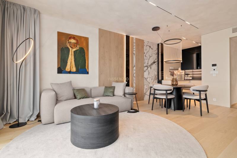 Living room with a sofa, round table, painting, and dining area in a three-room apartment.