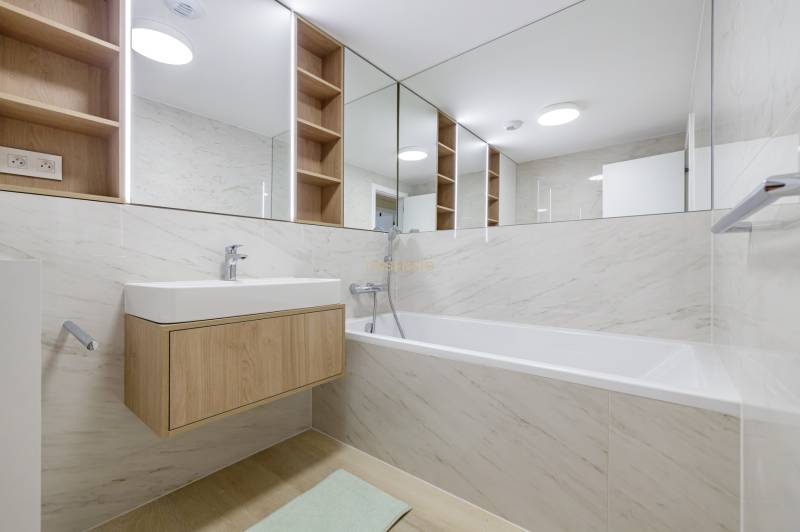 Bathroom with a bathtub, sink, and wooden shelves in a 3-room apartment.