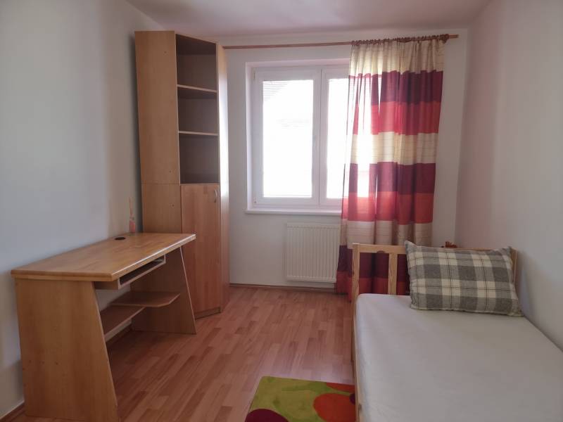 A room in a 4-room apartment with a wooden table, a wardrobe, and a bed with a pillow.