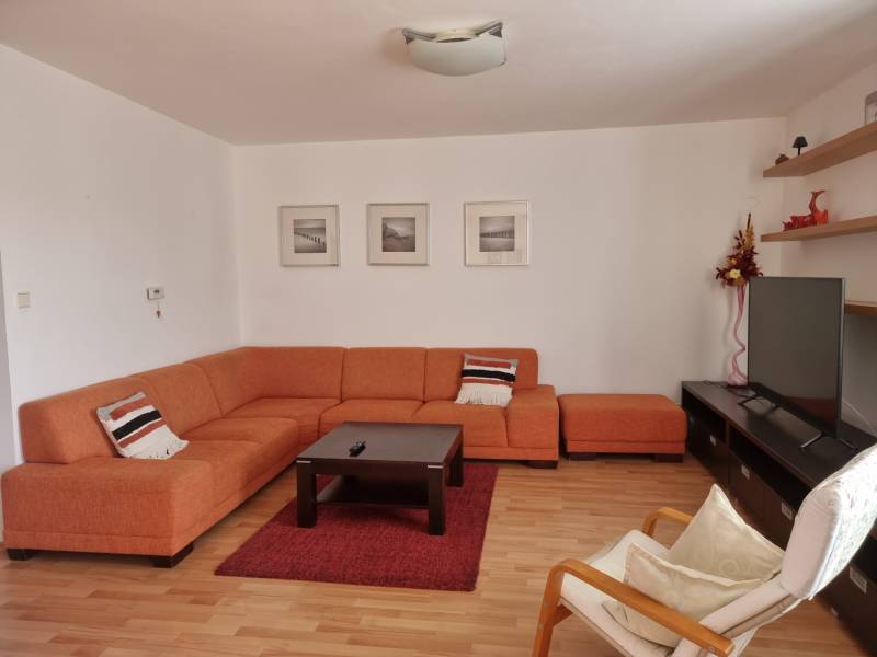 Living room of a 4-room apartment with an orange sofa, TV, and decorations on the shelves.