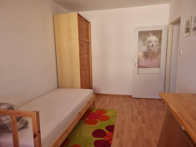 A simple room with a bed, a wooden wardrobe, and a colorful carpet in a 4-room apartment.
