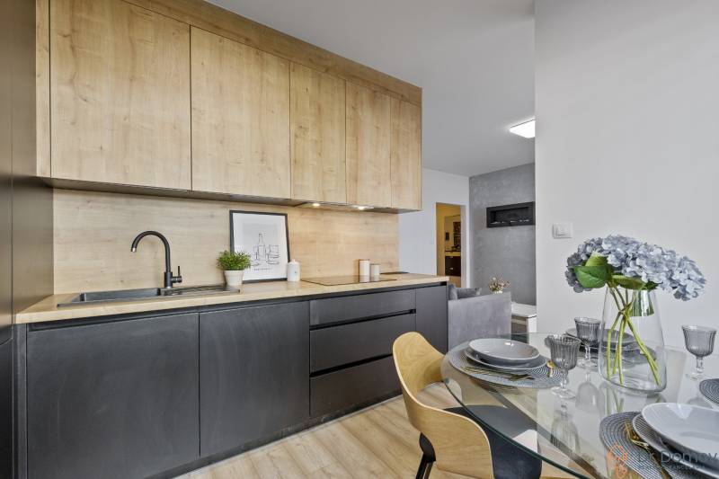 A kitchen in a 2-room apartment with wooden cabinets, a dining table with flowers.