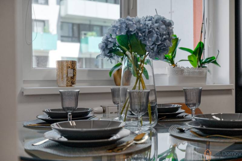 An elegantly set table with flowers in a 2-room apartment, glassware, and cutlery.