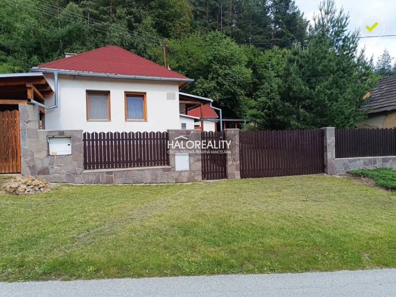 A cottage in Helcmanovce with a wooden fence and a manicured lawn surrounded by greenery.