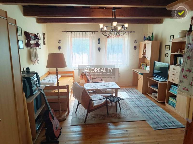 A cottage with a wooden ceiling, a sofa set, a guitar, shelves, and decorative items.