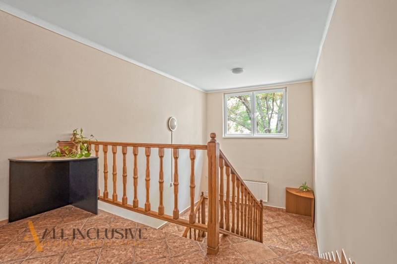 Interior of an office with a staircase, railing, window, and a plant on a corner cabinet.