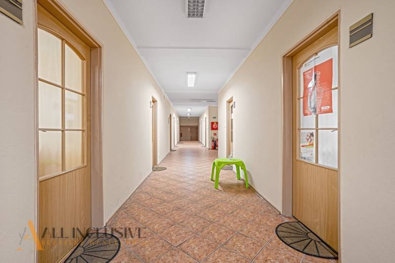 A corridor with doors, tiles, and a green chair in offices.