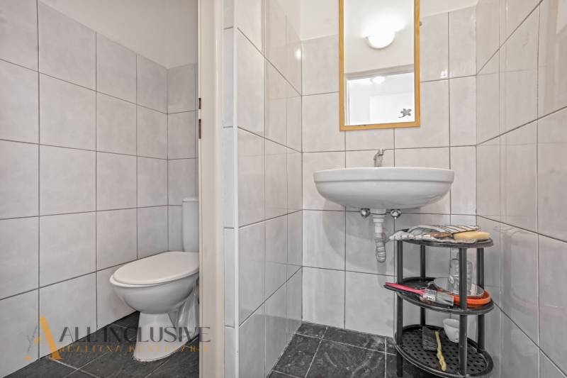 Bathroom in commercial premises with a sink, toilet, and shelf for accessories.