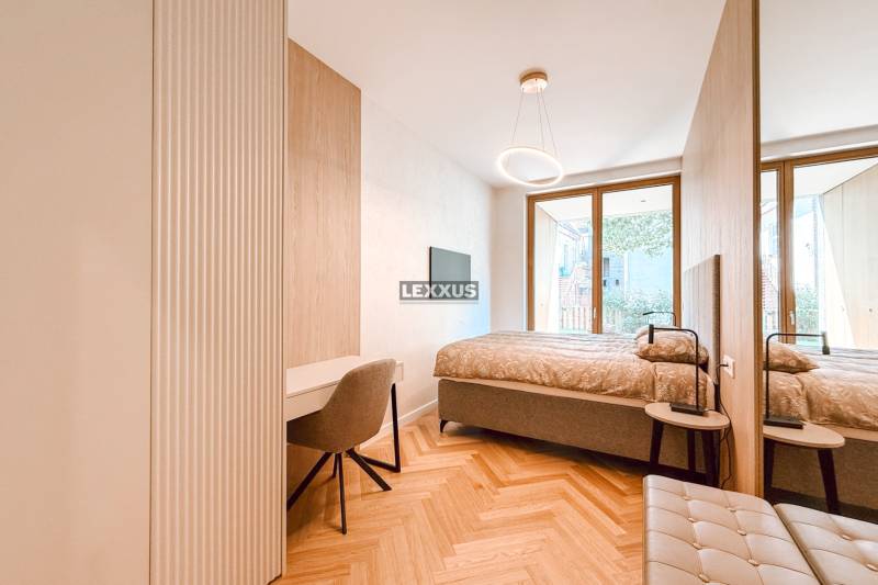 A bedroom with a desk and a chair in a four-room apartment, with a large window and wooden flooring.