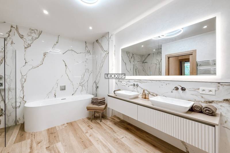A bathroom with a bathtub and double sink in a 4-room apartment, marble walls and wooden floor.