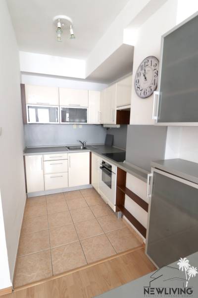 A kitchen in a 2-room apartment with tiles, appliances, and a wall clock.