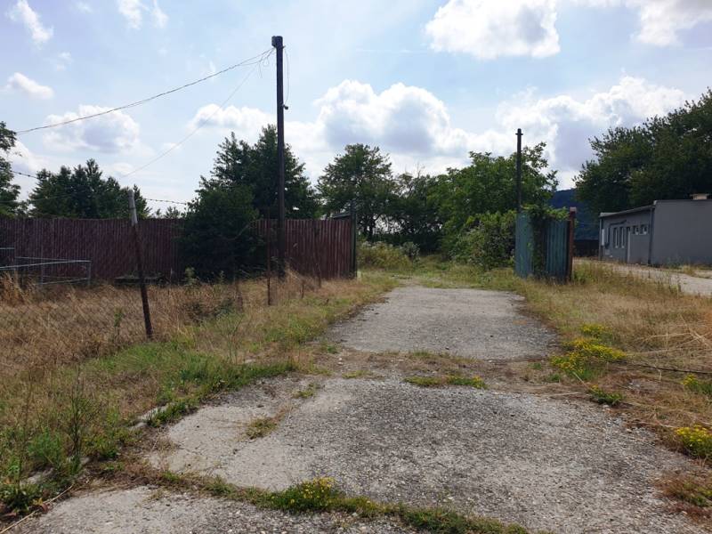 The reinforced road leads through commercial properties in Trenčianske Bohuslavice, surrounded by greenery.