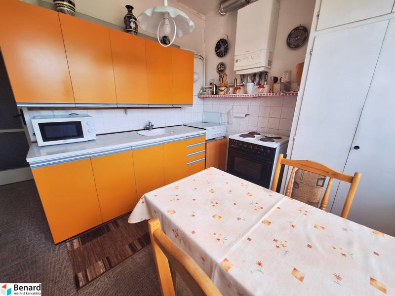 The kitchen of a 2-room apartment with yellow cabinets and a dining table.