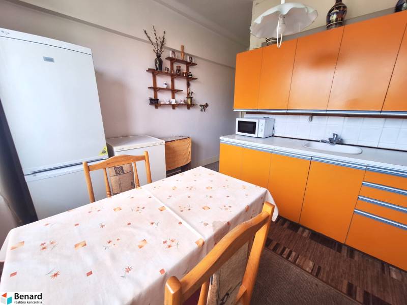 A kitchen in a 2-room apartment with an orange kitchen unit, a white refrigerator, and a dining table.