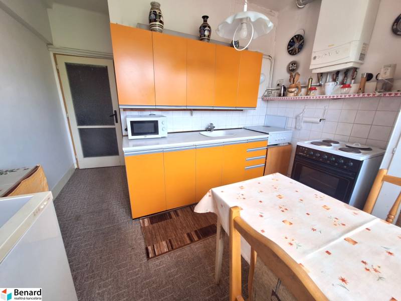 A kitchen with an orange countertop and a dining table in a 2-room apartment.