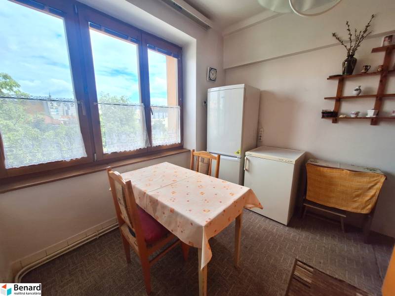 Dining room of a 2-room apartment with a table, refrigerator, and a display cabinet on the wall.