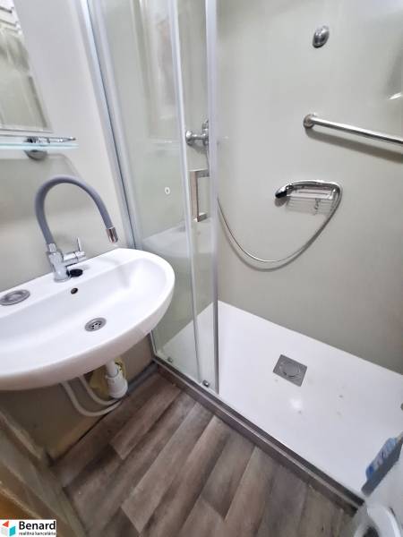 A bathroom in a 2-room apartment with a sink, shower, and laminate flooring.