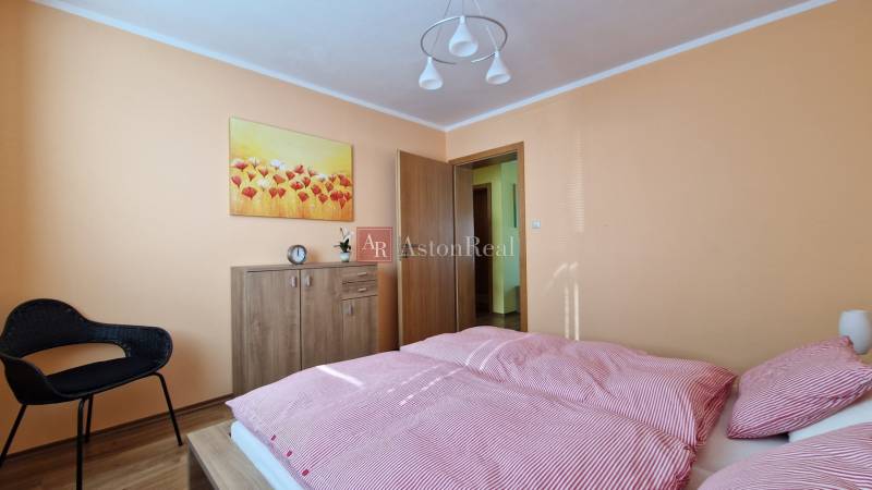 Bedroom in a Holiday Apartment with a bed, wardrobe, armchair, and a painting of flowers.