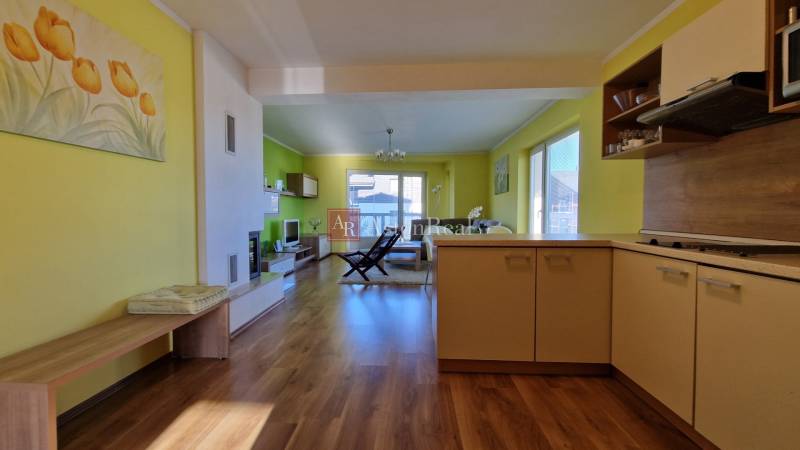 Interior of a holiday apartment with wooden flooring, an armchair, and a kitchen unit in warm colors.