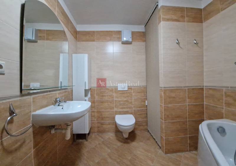 Bathroom in a holiday apartment with a sink, mirror, and toilet, tiled with brown tiles.