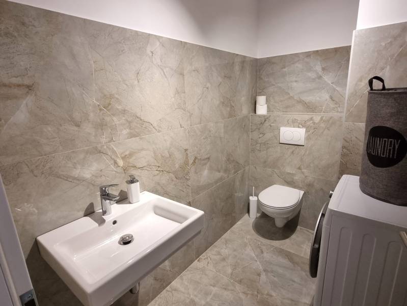 A bathroom in a 3-room apartment with a sink, toilet, and washing machine, tiled.