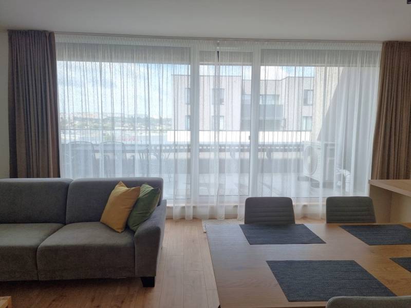 Living room of a 3-room apartment with a sofa, dining table, and a view of the balcony.