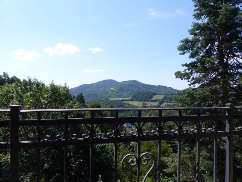 The view from the cottage of the mountain range in Štiavnické Bane, framed by metal railings and trees.