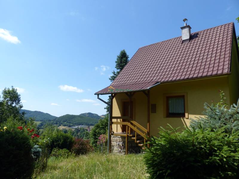 A cottage in Štiavnické Bane, surrounded by greenery and with a view of the hills in the background.