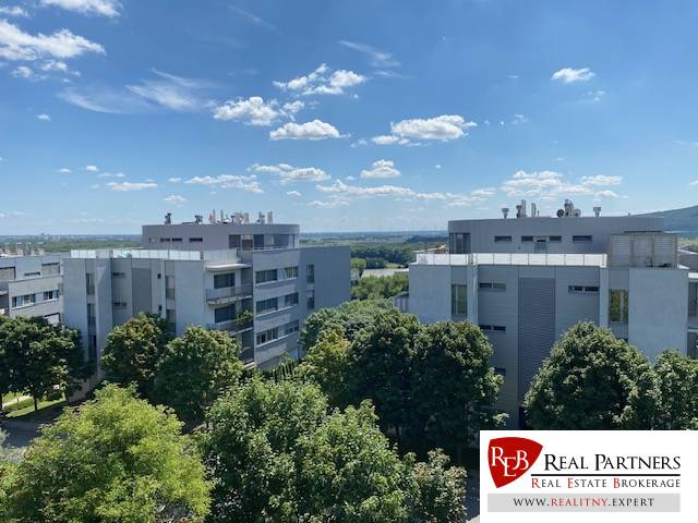 A view of modern apartment buildings in Bratislava - Karlova Ves surrounded by greenery and a blue sky.