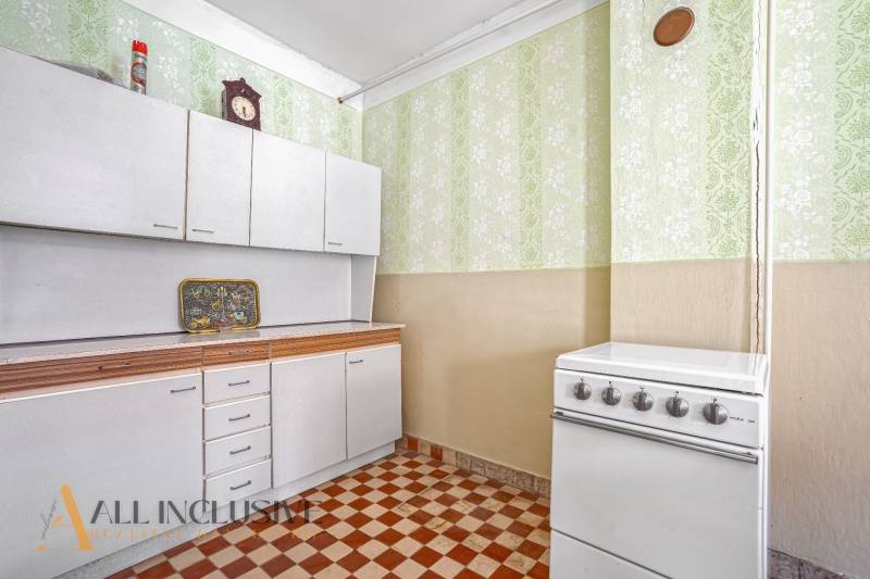 A kitchen with white cabinets, a stove, and patterned green wallpaper in a family house.