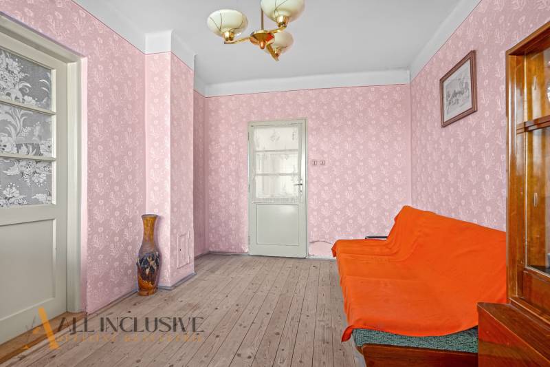 A room in a family house with an orange sofa, pink wallpaper, and a vase on a wooden floor.
