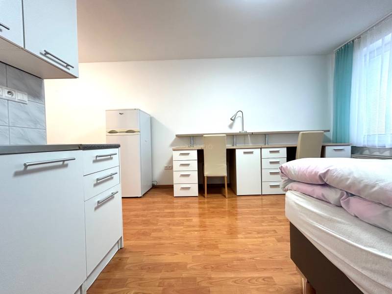 A studio apartment with a bright interior, a kitchenette, a table, two chairs, and a bed.