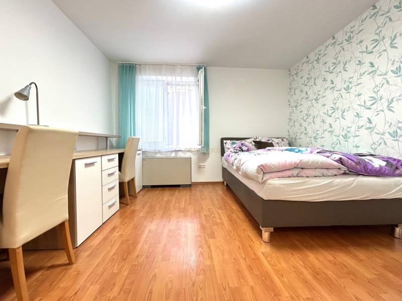 A studio apartment bedroom with a work desk, bed, and decorative wallpaper.