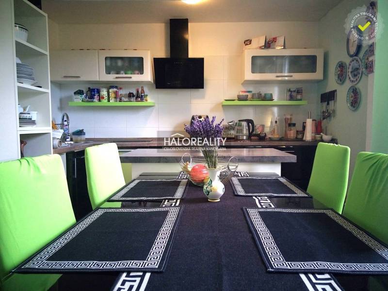 Kitchen in a family house with a dining table, green chairs, and kitchen equipment.