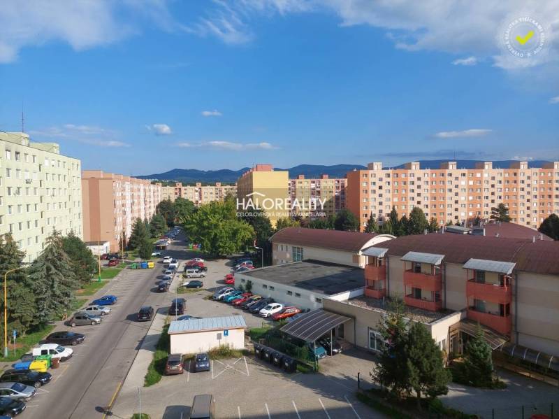 A view of the housing estate in Prievidza with panel buildings and parked cars.