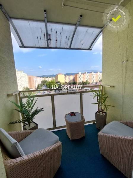 A balcony of a 3-room apartment with rattan furniture and a view of the housing estate in Prievidza.