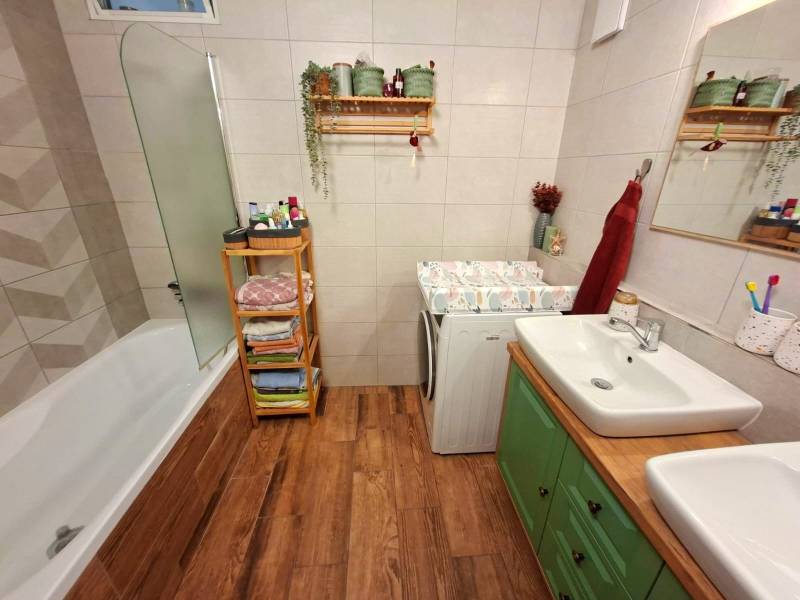 A bathroom in a 4-room apartment with a bathtub, sink, and washing machine on a wooden floor.
