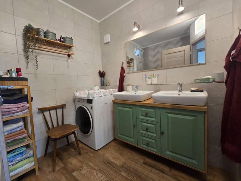 The bathroom in the four-room apartment has two sinks, a washing machine, and shelves with towels.