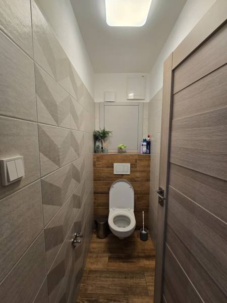 A toilet in a 4-room apartment with wooden paneling and white tiles.