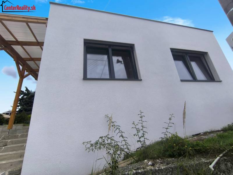 A family house in Malé Kršteňany with a pair of large windows and a wooden shelter.