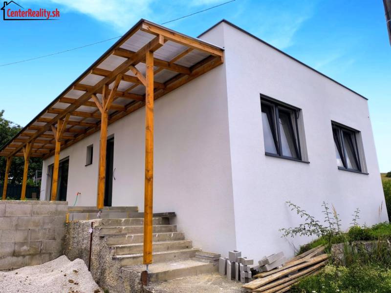 A family house in Malé Kršteňany with a wooden extension and concrete stairs, blue sky.