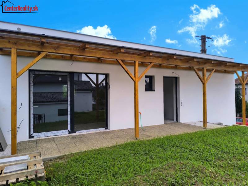 A family house in Malé Kršteňany with a wooden pergola and lawn on a sunny day.