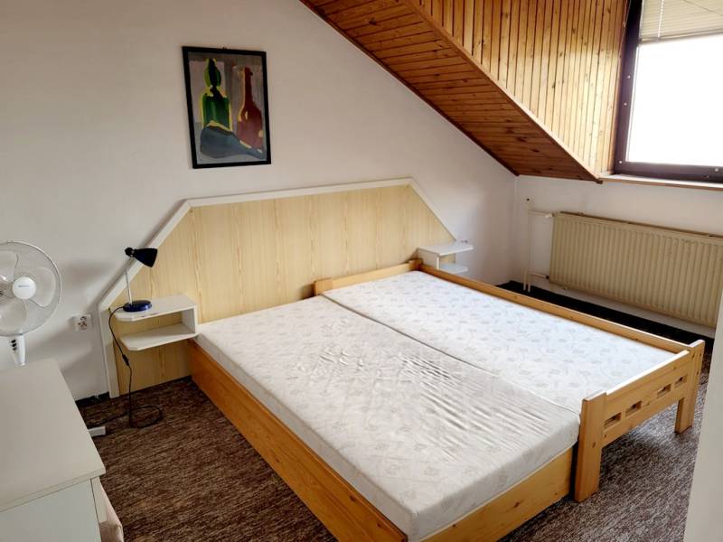 A double bed under a slanted ceiling in a 2-room apartment with a painting on the wall.