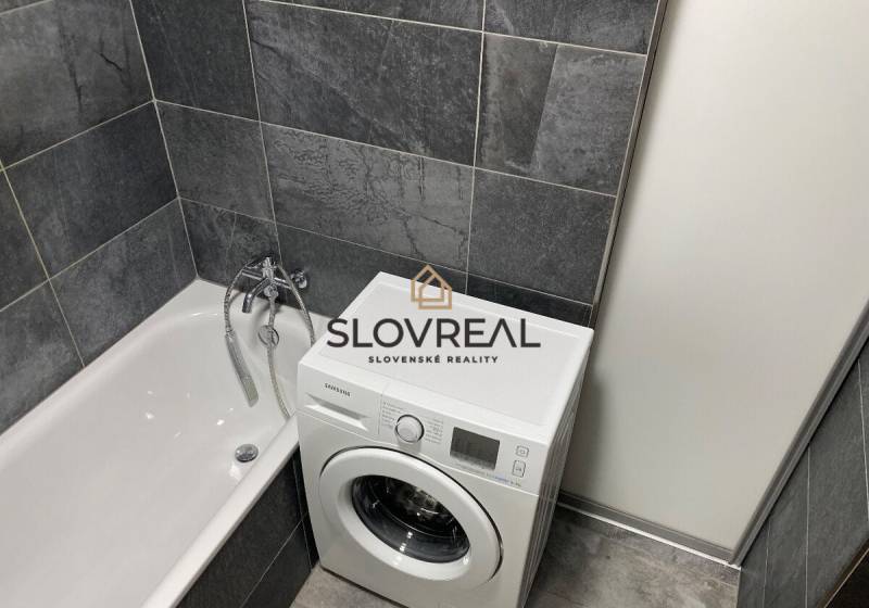 A bathroom in a 4-room apartment with a bathtub and a washing machine in dark gray tiles.