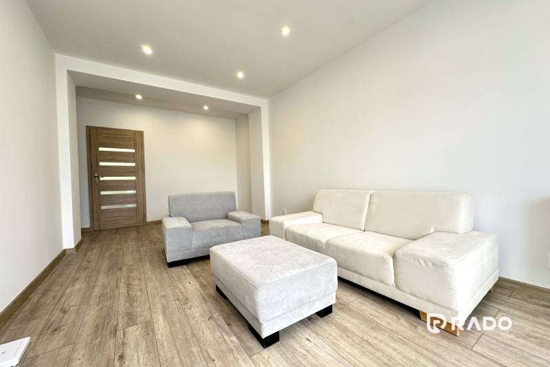 A bright living room in a two-room apartment with beige furniture and wooden flooring.